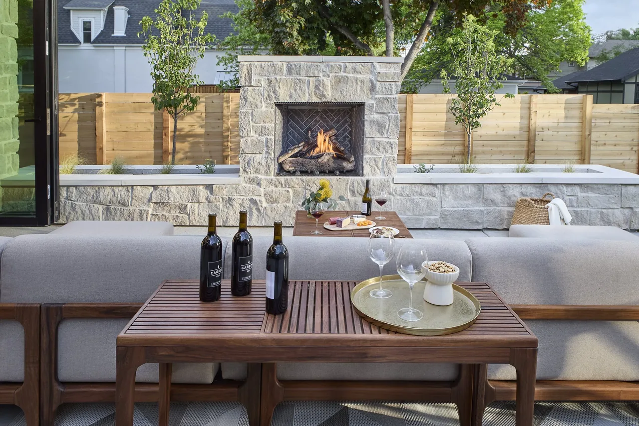 Patio with stone fireplace and wooden furniture arranged for outdoor living.