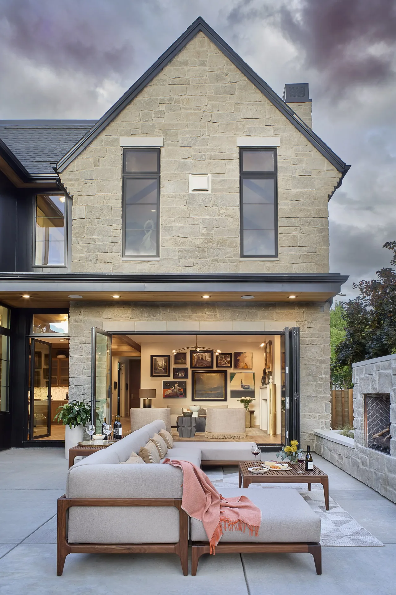 Stone rear exterior of a modern house with bi-fold glass doors opening to an outdoor seating area.