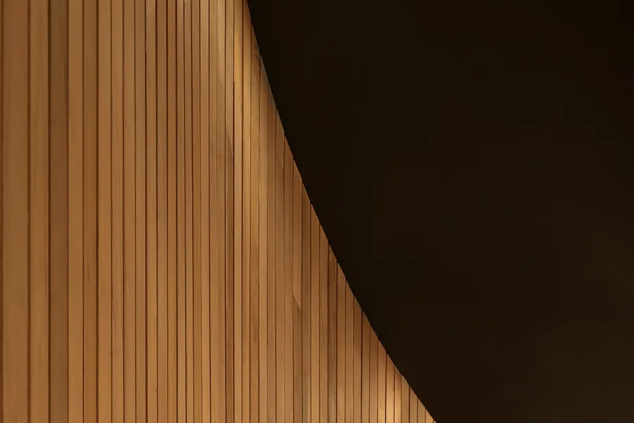 Curved vertical wood wall with an angled dark ceiling at Grennoch Residence by CONTENT Architecture.