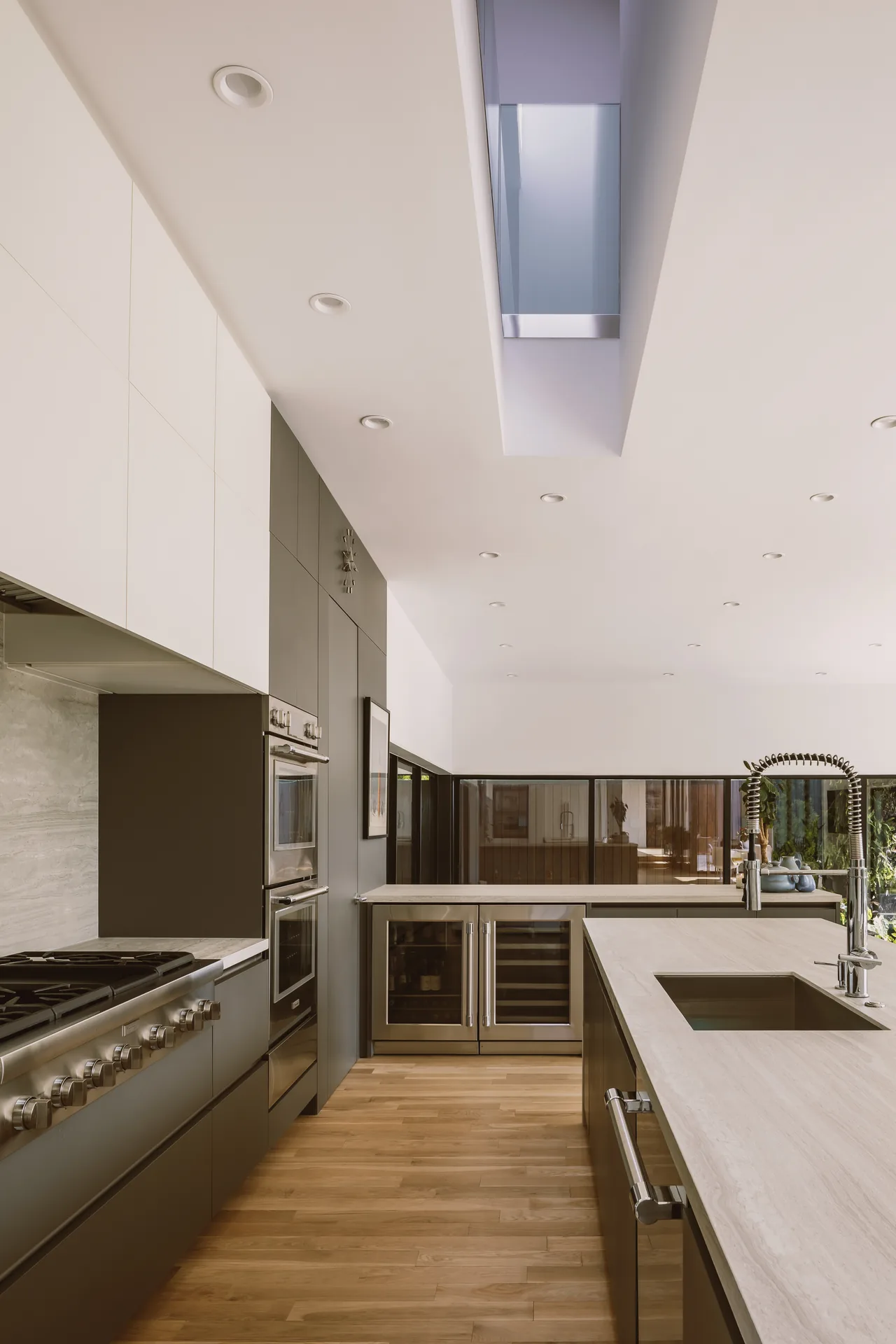 The Grennoch Residence kitchen features wood flooring, integrated appliances, and a skylight for natural light.