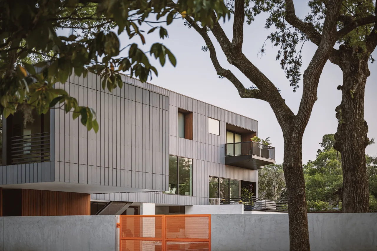 The Grennoch Residence features vertical groove siding, large glass windows, and a cantilevered balcony with a concrete boundary wall and orange gate.