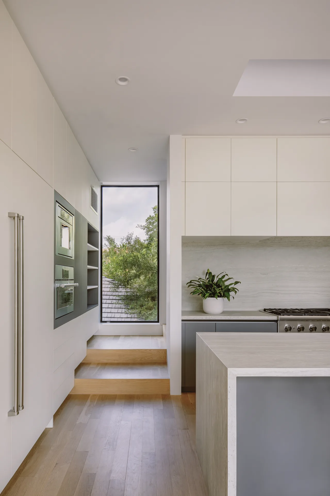 The Grennoch Residence kitchen by CONTENT Architecture shows clean lines with white cabinets, light wood floors, and integrated appliances.