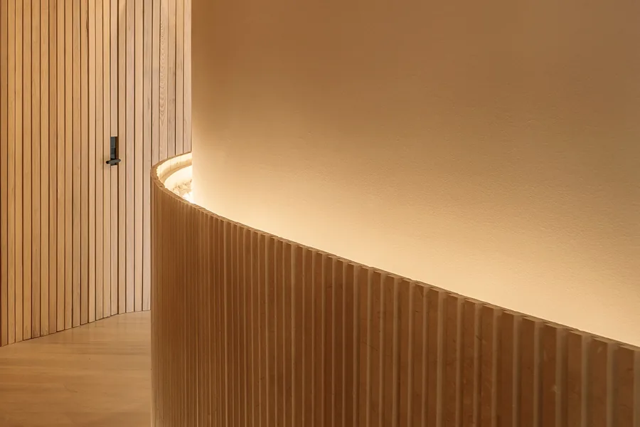 Curved wall with vertical wood slats and integrated lighting detail in the Grennoch Residence hallway.