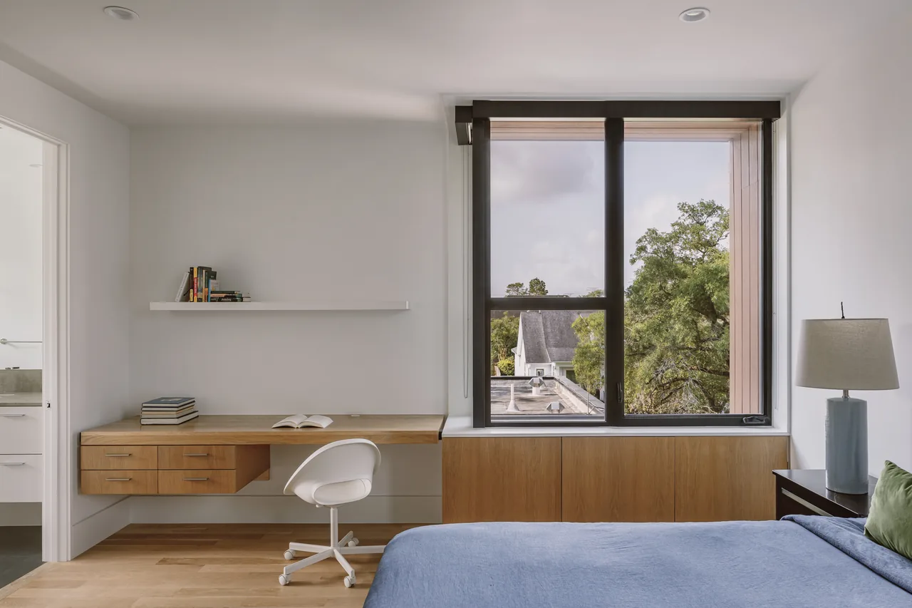 Bedroom in the Grennoch Residence with a floating wood desk and large window overlooking trees.