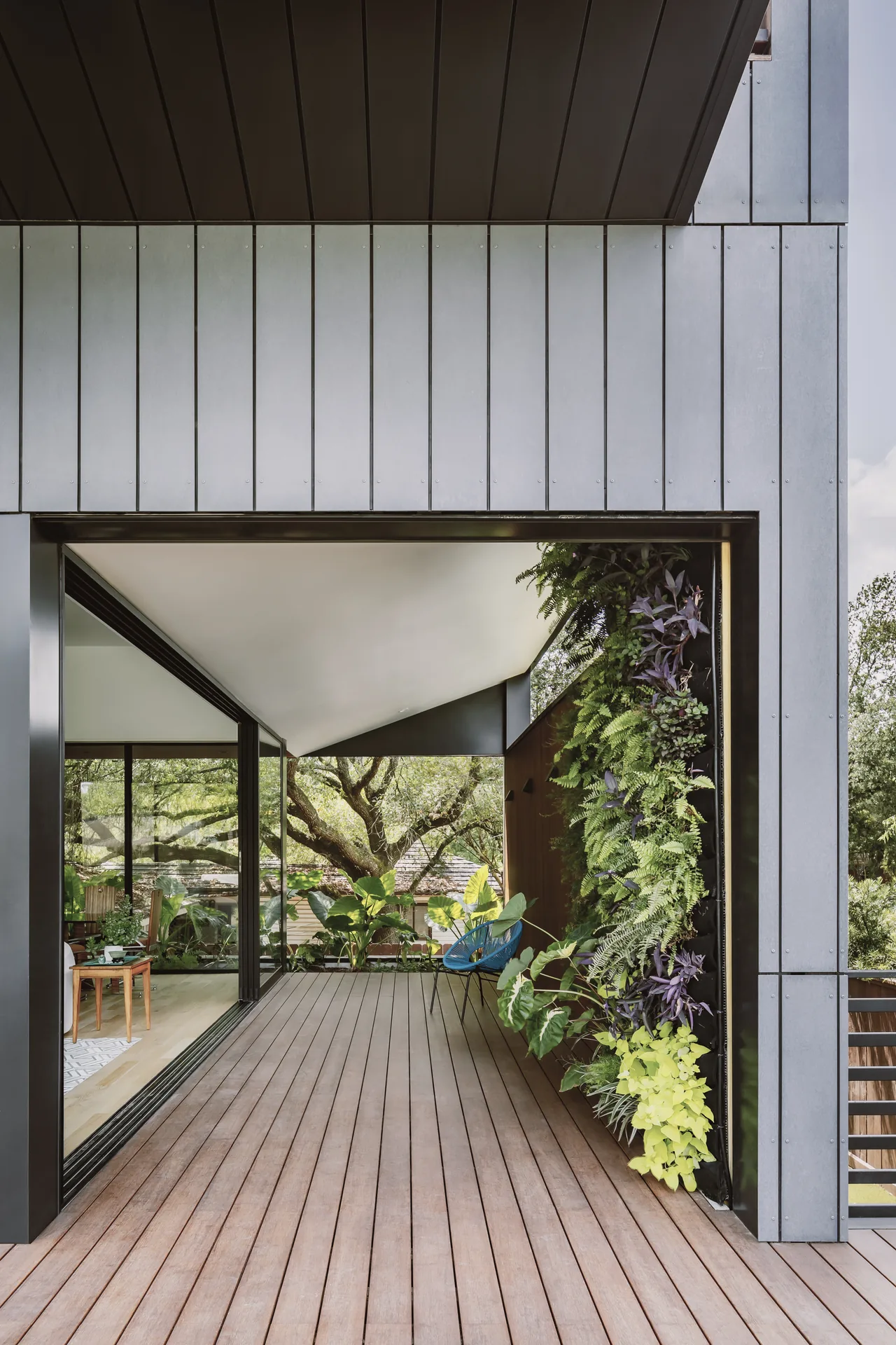 Deck with wood flooring and vertical plant garden next to large glass walls opening to an interior living area