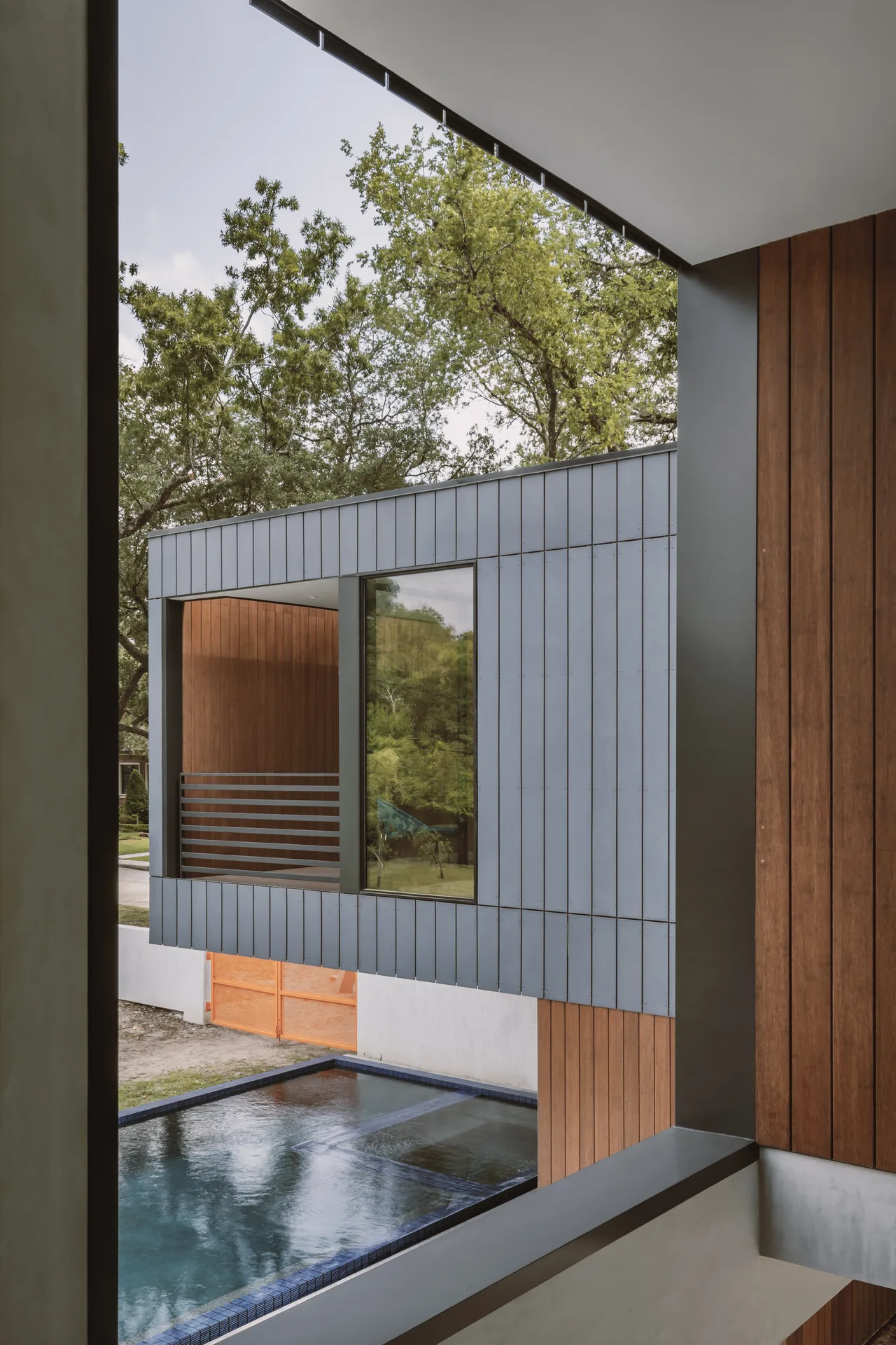 Grennoch Residence exterior with vertical metal and wood siding above a reflecting pool, highlighting a modern architectural style.