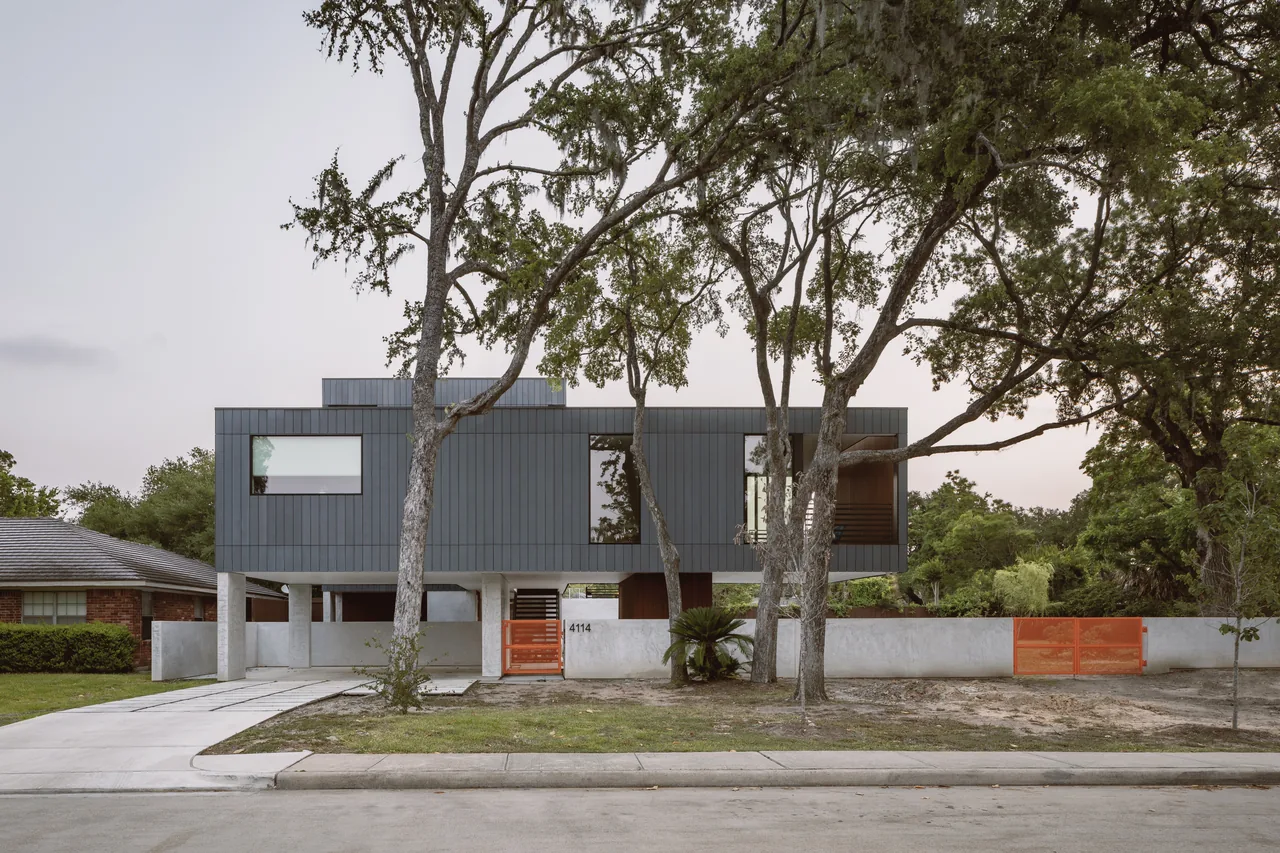 Grennoch Residence by CONTENT Architecture features an elevated boxy design with vertical gray siding and vibrant orange gates.