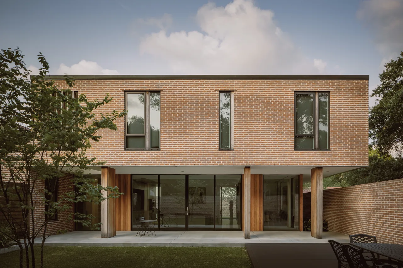 Rice Magister House features a brick exterior with wood-paneled columns and floor-to-ceiling glazing on the first floor.