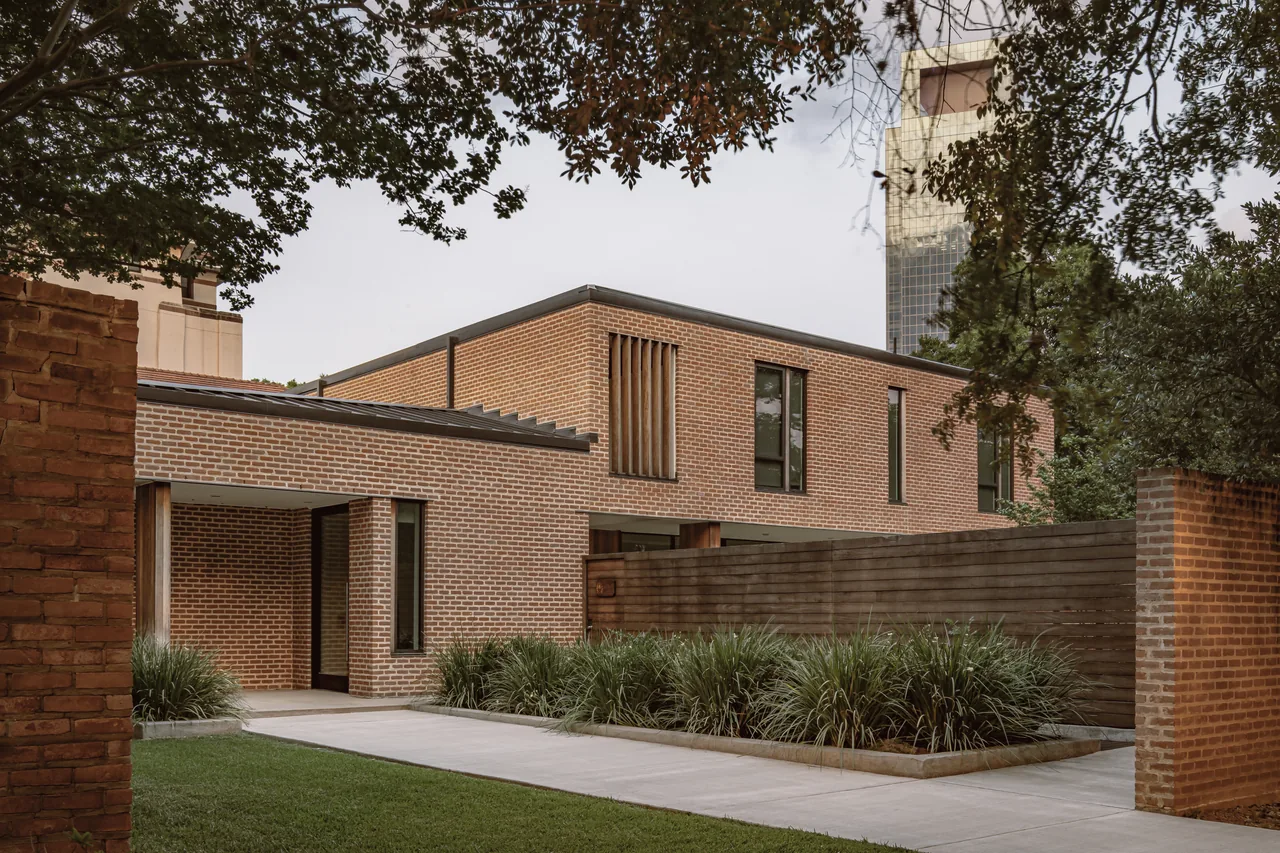 Rice Magister House features brick walls with vertical wooden window slats and a wood privacy fence enclosing a small garden area.