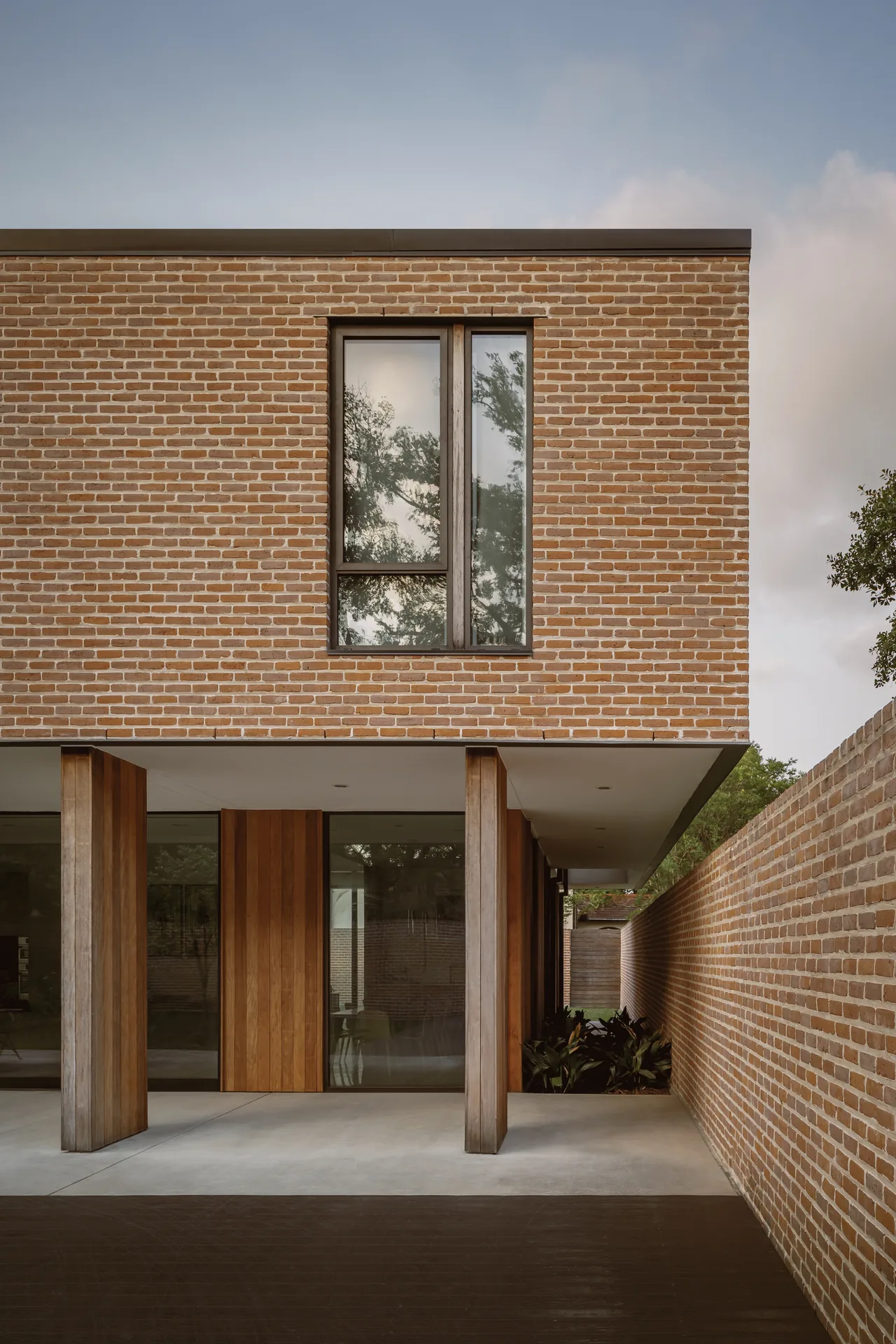 Exterior view of the Rice Magister House showing brick facade, vertical window, and wood-paneled columns by CONTENT Architecture.