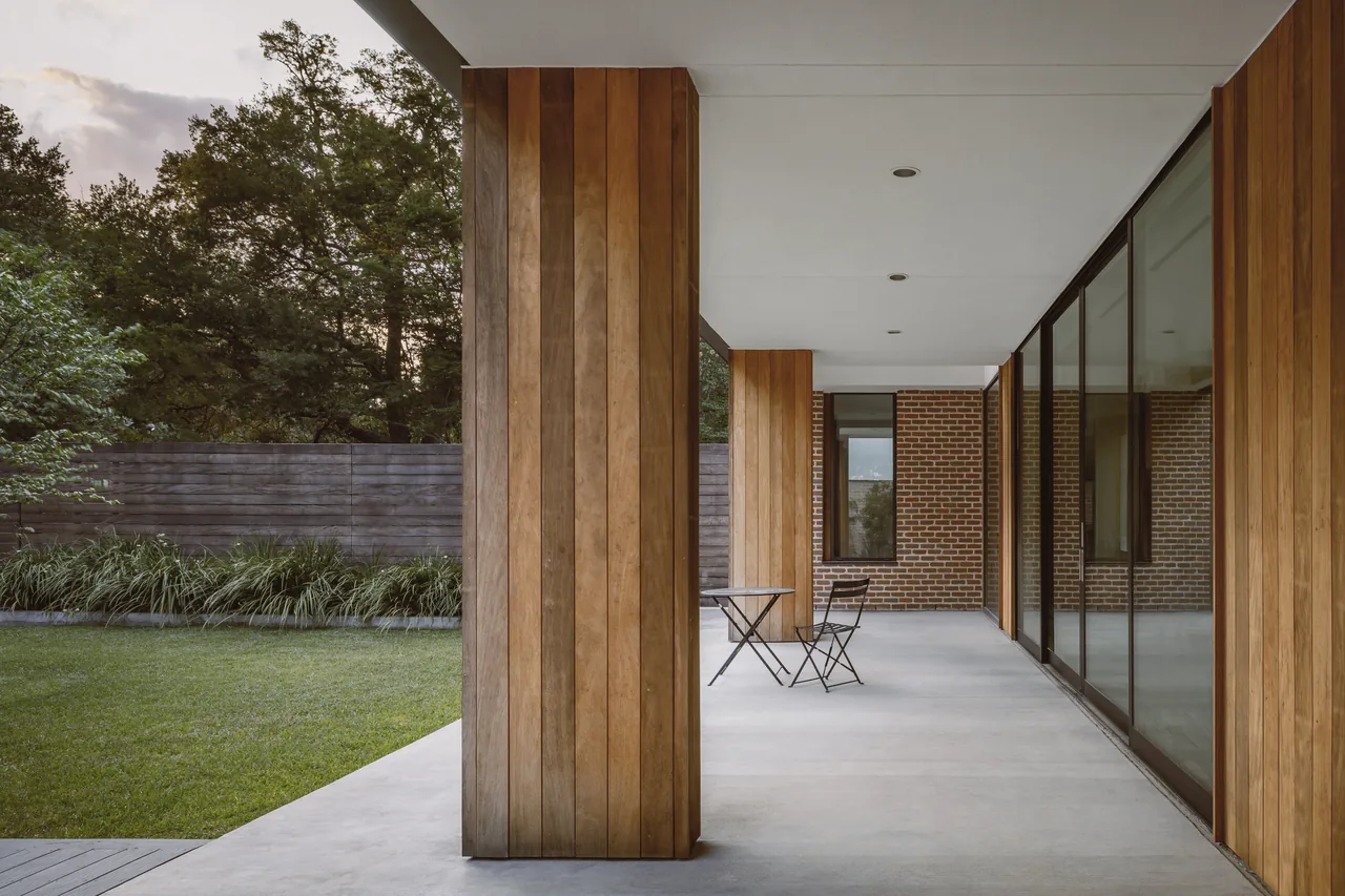 Covered patio features wood-paneled columns, concrete floor, and large sliding glass doors opening to a garden lawn.