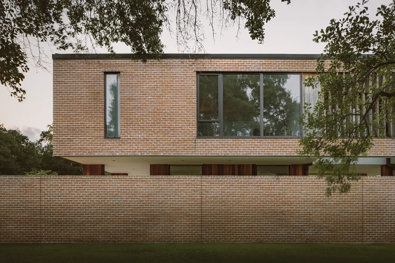 The Rice Magister House features brick exterior walls with large black-framed windows and a brick privacy wall surrounding the lower level.