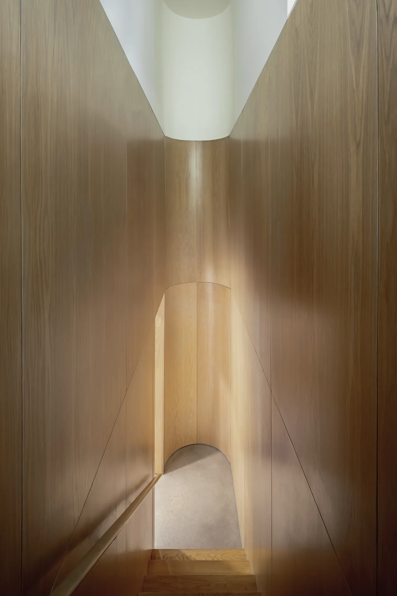 Curved wood-paneled staircase with natural light from a skylight above.