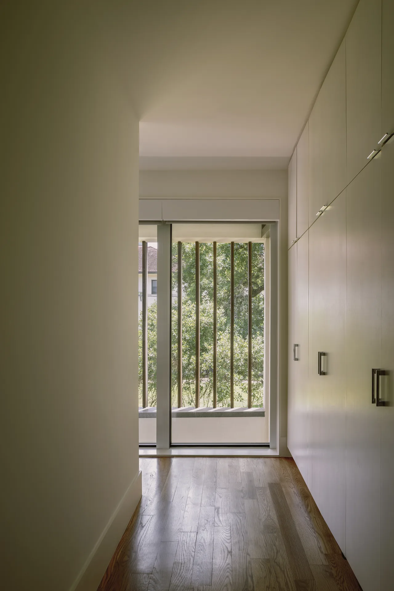 Narrow hallway with built-in storage and vertical wooden slats outside the glass door in the Rice Magister House.