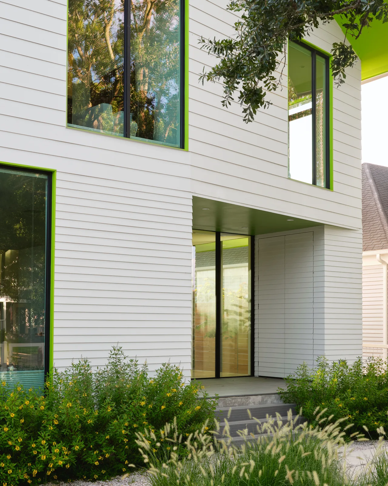 Allston Residence features white siding with bright green window trim and large vertical windows for natural light.