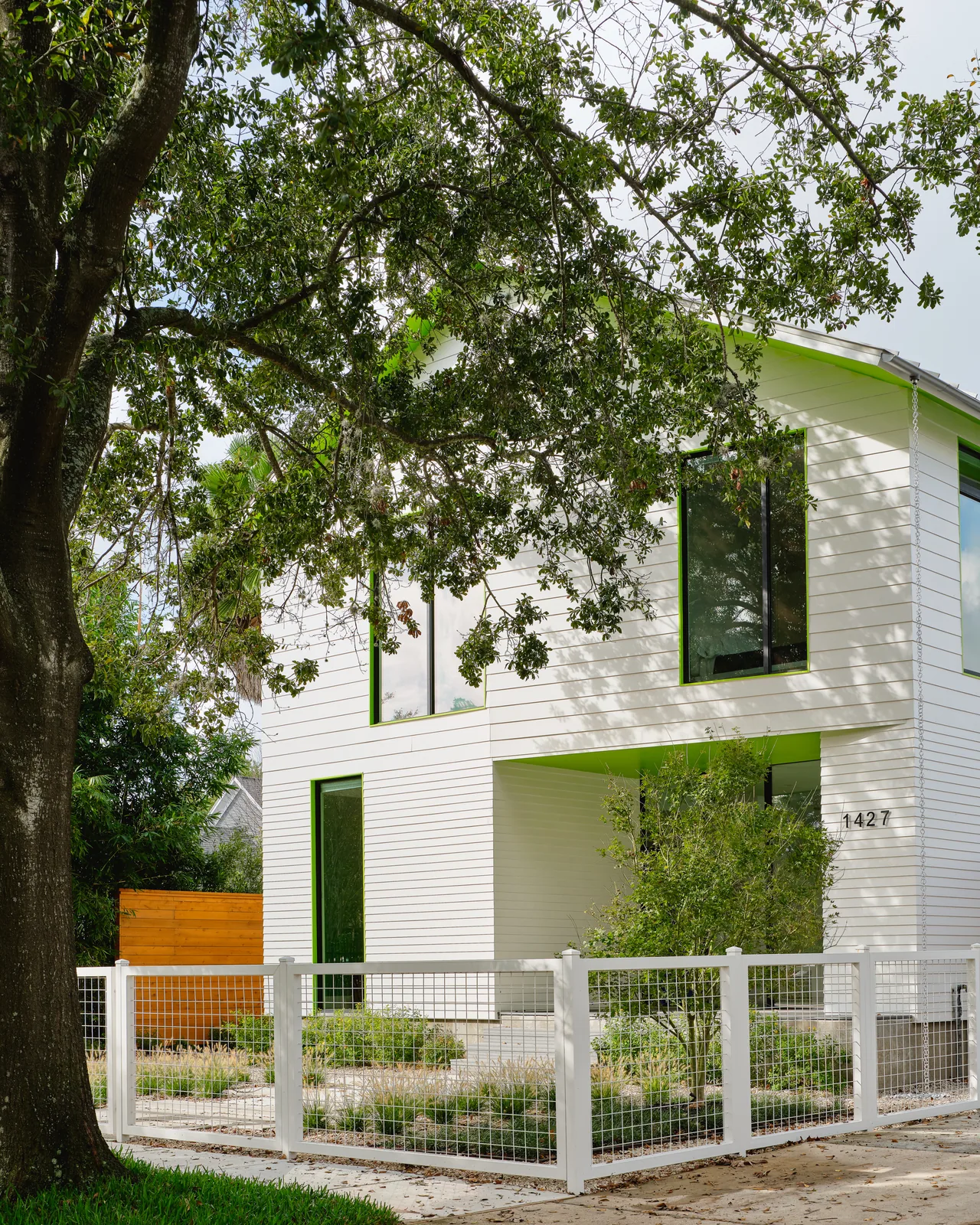 The Allston Residence by CONTENT Architecture features white siding with green window trim and a fenced front yard.