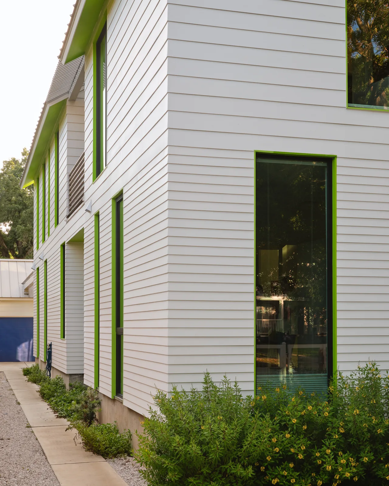 Allston Residence features white horizontal siding with green window frames and a blue garage door.