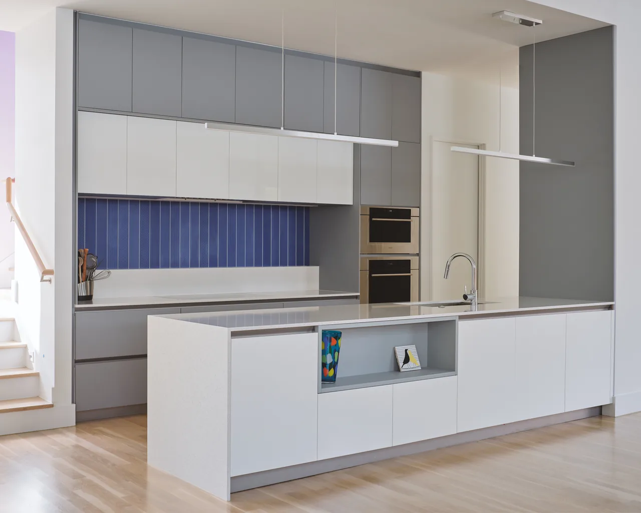 Allston Residence kitchen by CONTENT Architecture features gray and white cabinetry with a blue tile backsplash and a white island with open shelving.