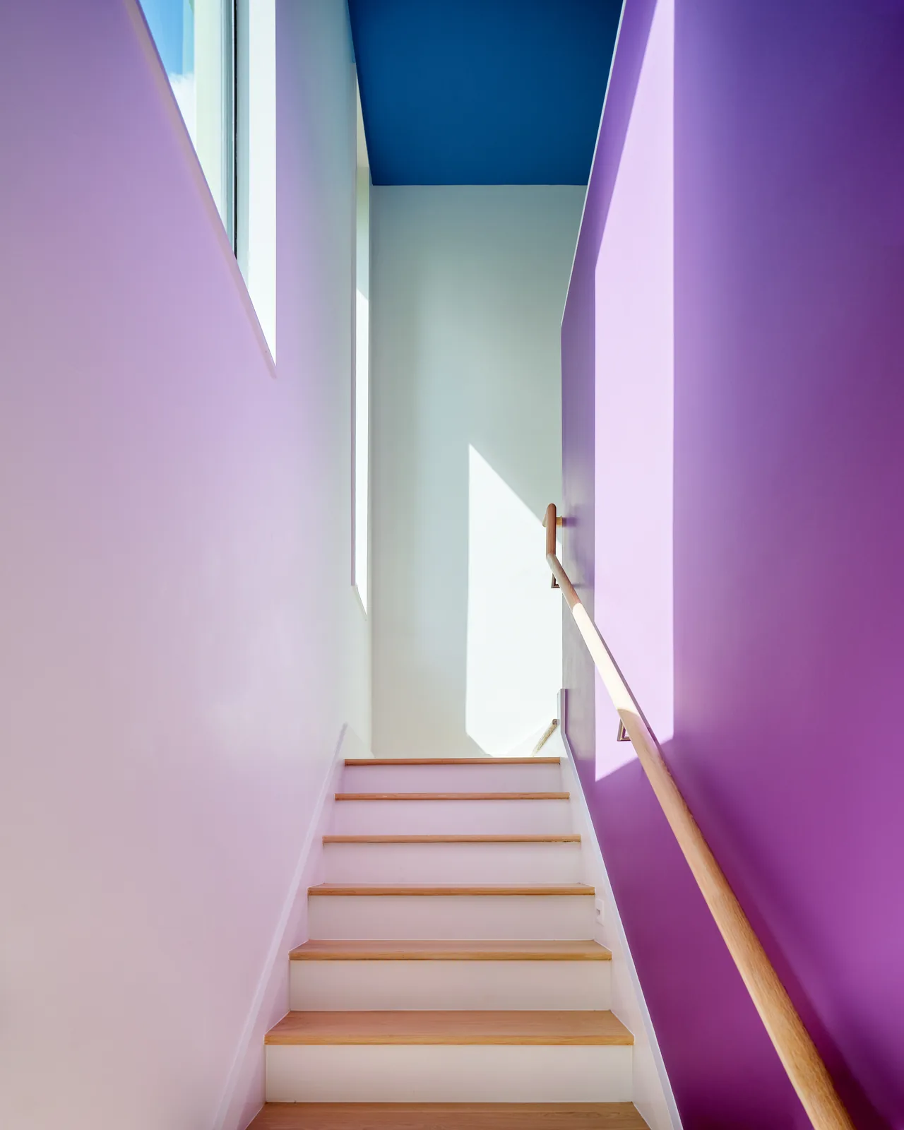Stair space with white walls, a purple accent wall, natural wood stair treads and handrail, and a blue ceiling.