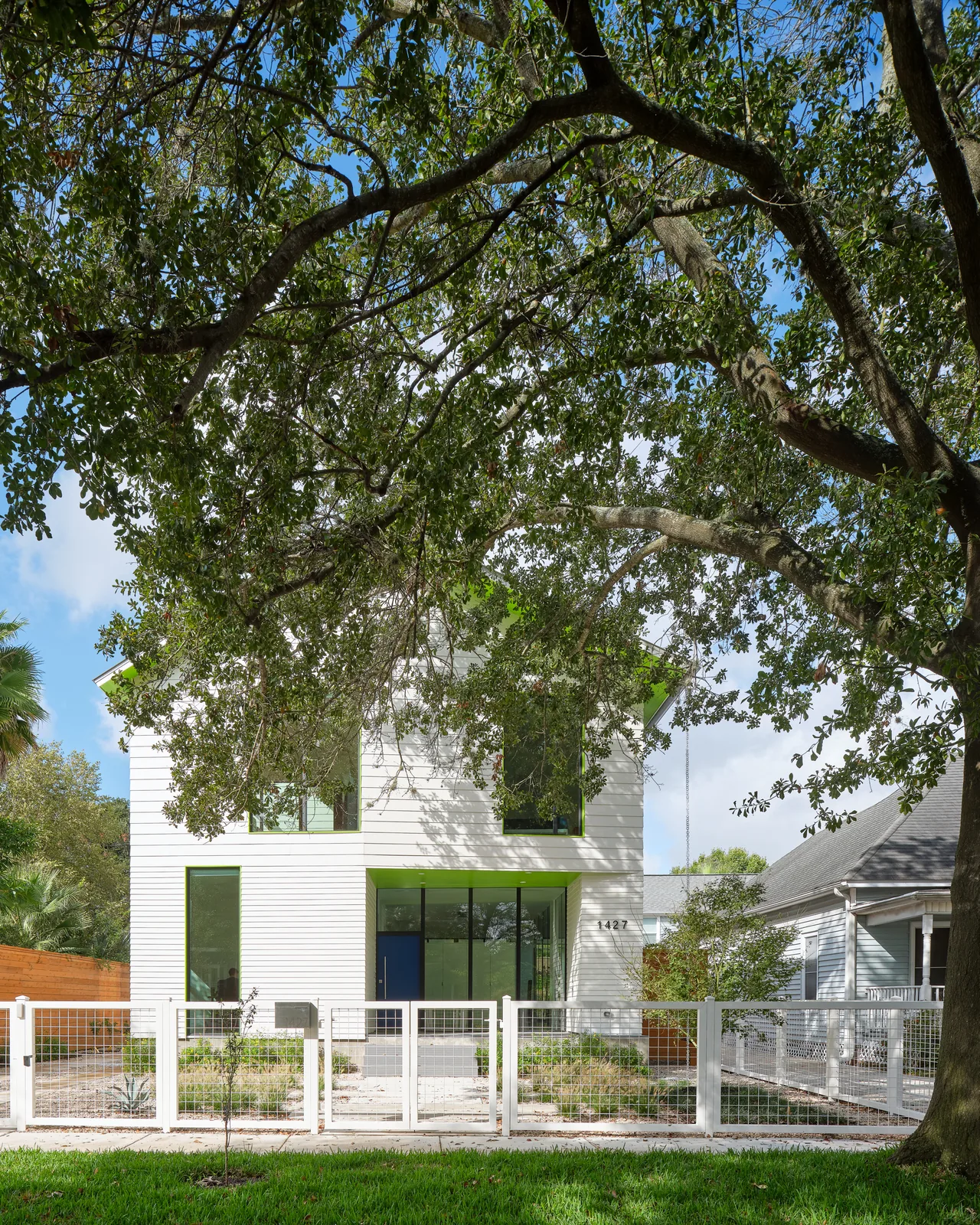 Allston Residence shows a modern exterior with green window trims, white siding, and a white fence under mature tree cover.