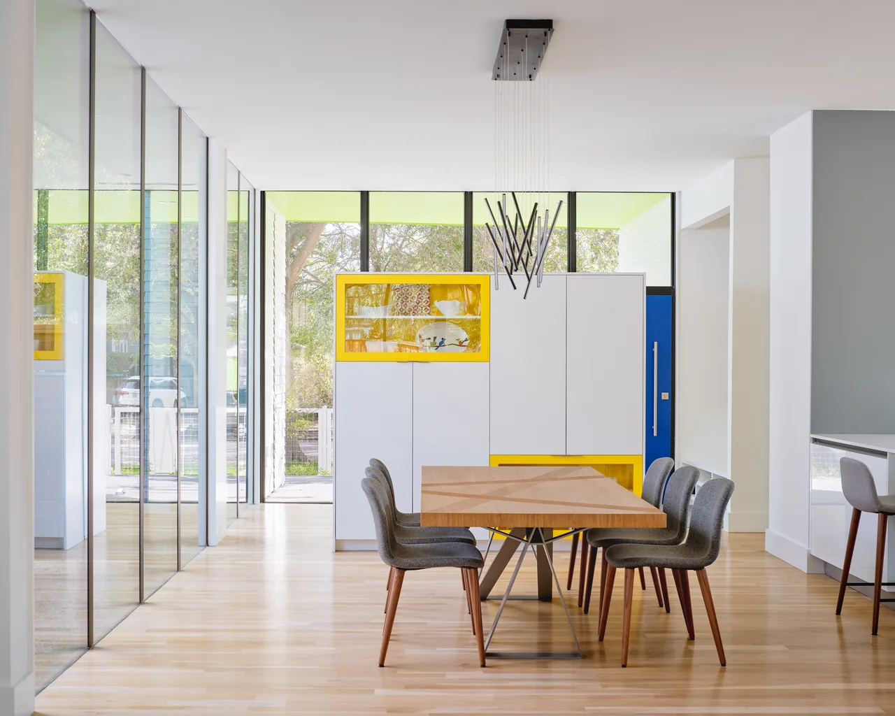 Dining space featuring a wood table and gray chairs illuminated by large vertical windows and accented cabinetry.