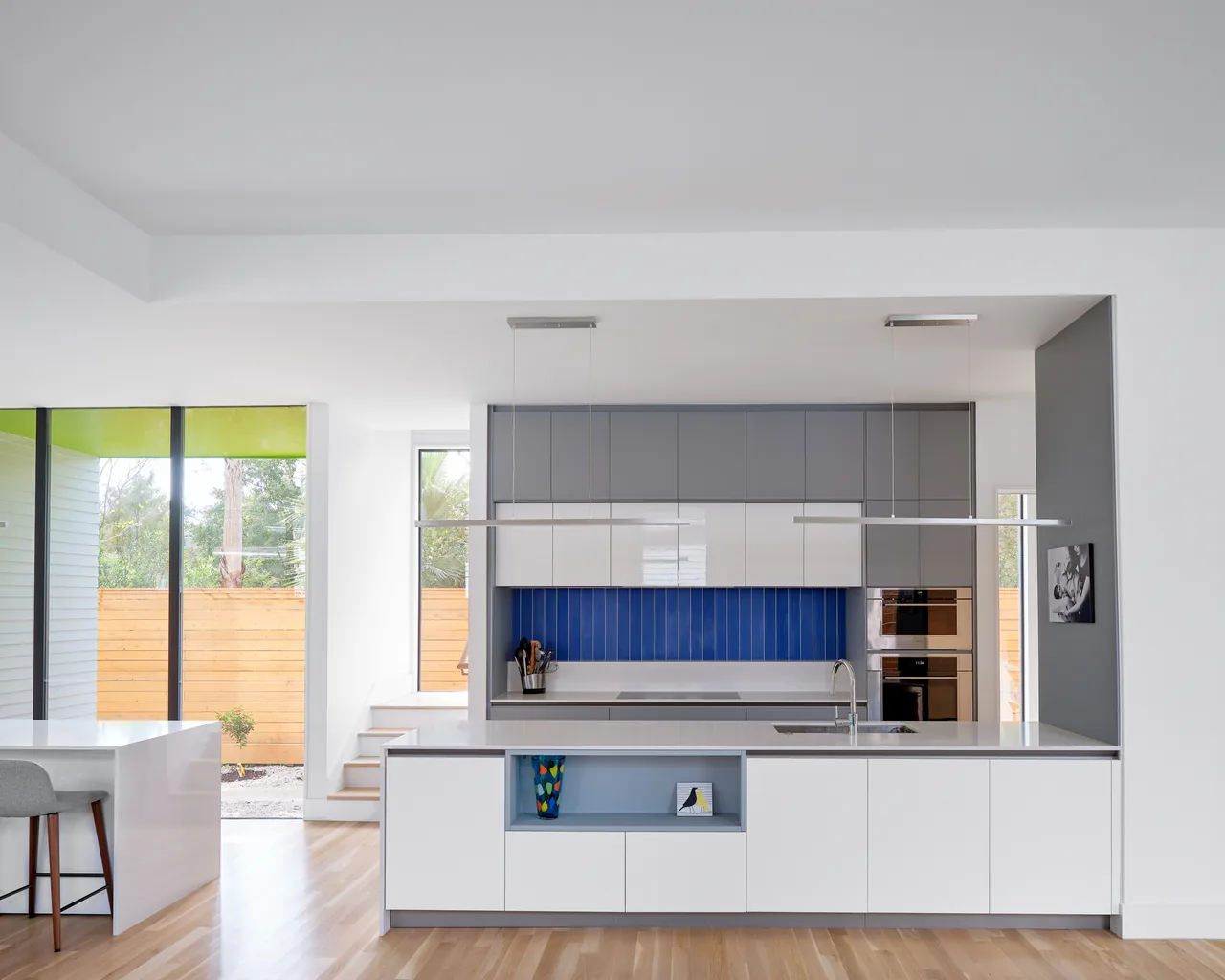 The Allston Residence kitchen features a bold blue backsplash with white and gray cabinets in a contemporary style.