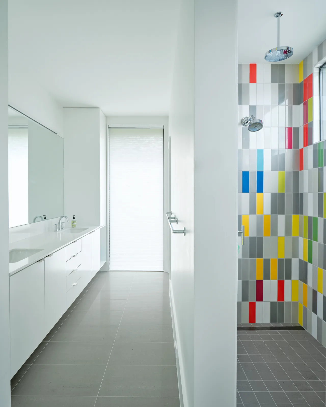 Bathroom featuring a white vanity and a walk-in shower with multicolored rectangular tiles and dual shower heads.