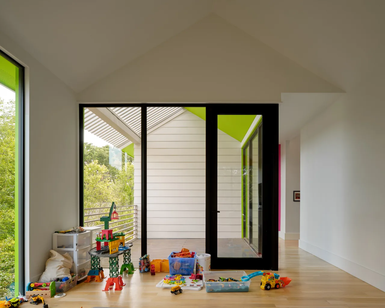 Play area with toys on floor near black-framed sliding door and bright green window trim at Allston Residence.
