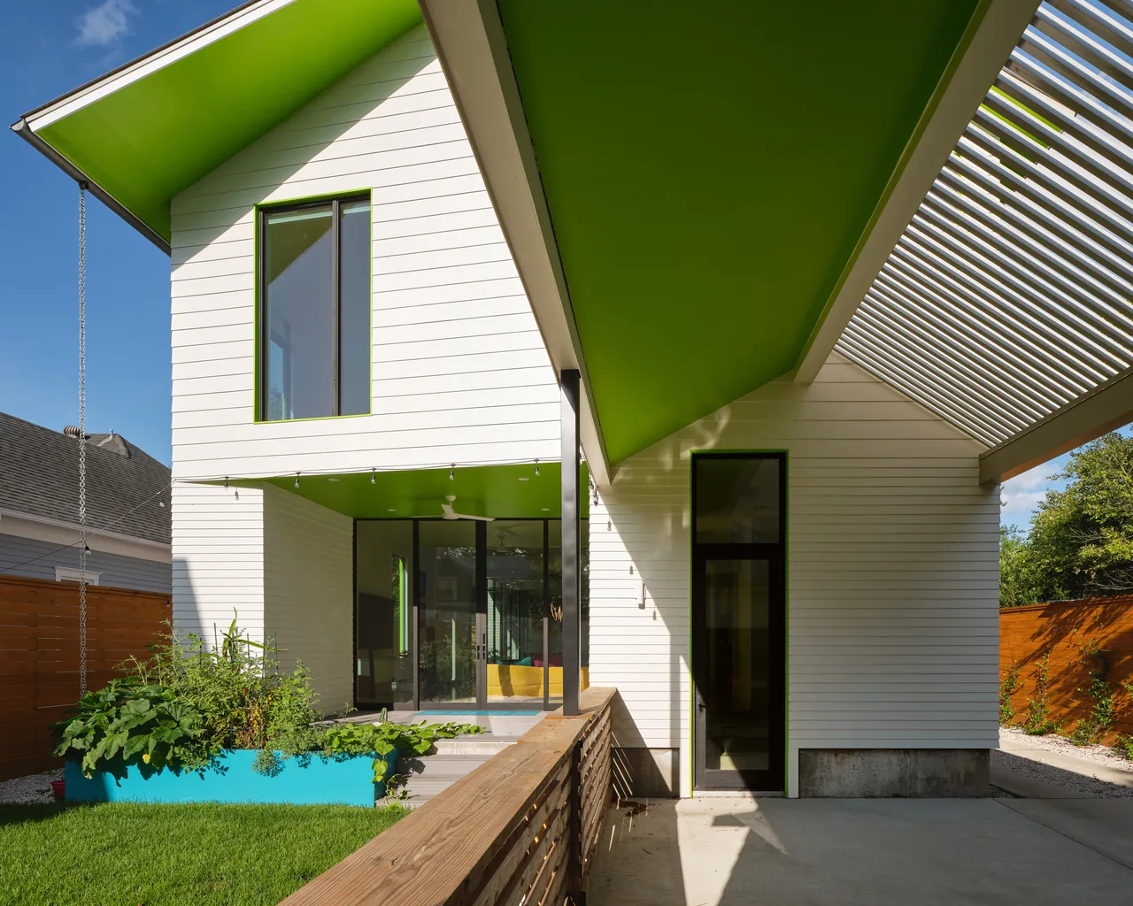 The Allston Residence features a distinctive green roof soffit, white siding, and integrates daylighting design with narrow vertical and rectangular windows.