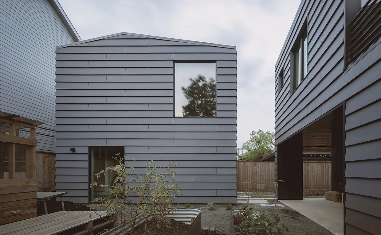 Two buildings clad in horizontal metal siding with minimal windows and a planted garden space between them.