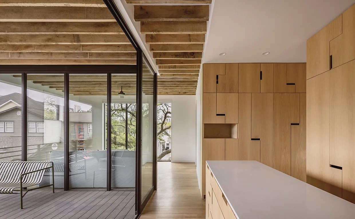Kitchen with wood veneer cabinets and island next to an enclosed patio with metal seating and exposed ceiling beams.