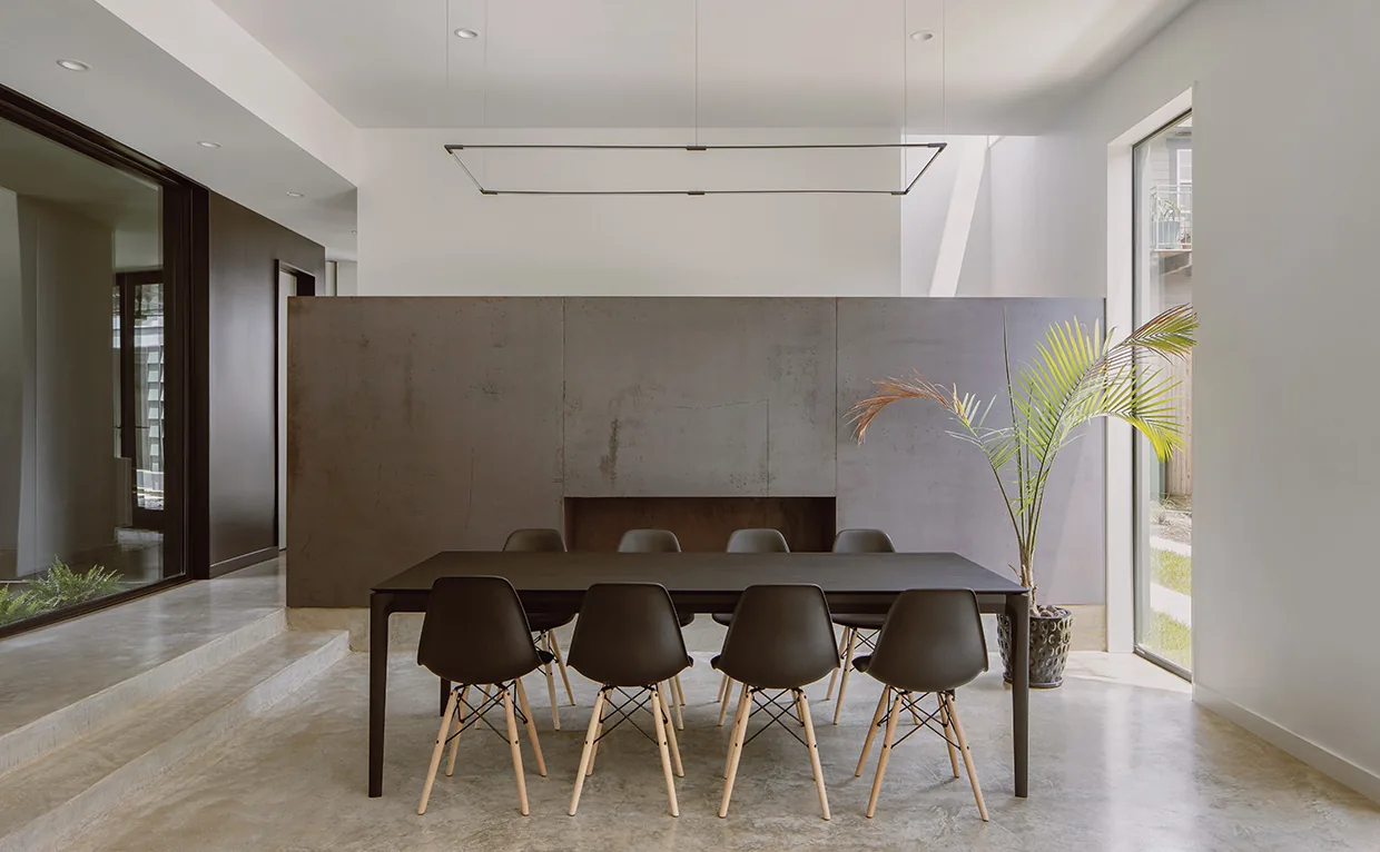 Dining area with black table and chairs on polished concrete floor beside large window.