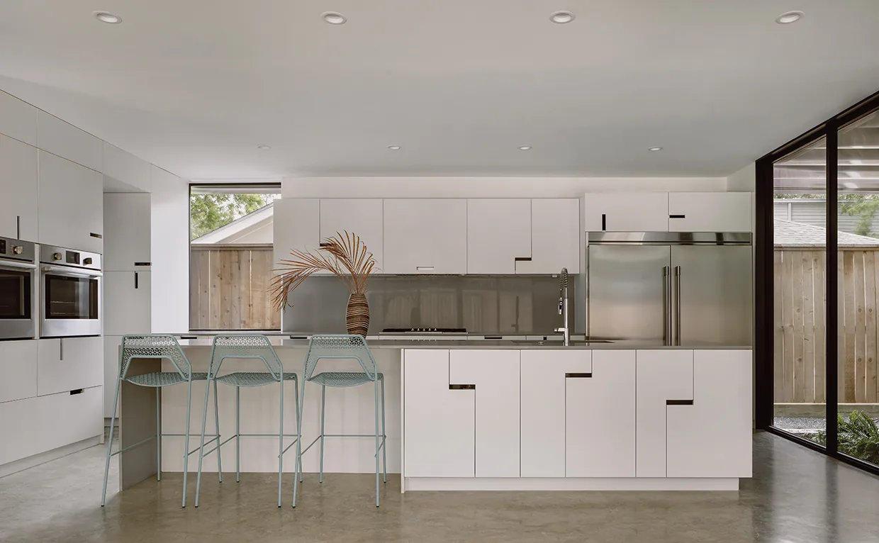 Contemporary kitchen with minimalist white cabinets, built-in stainless steel double ovens and refrigerator, and a central island with barstools.