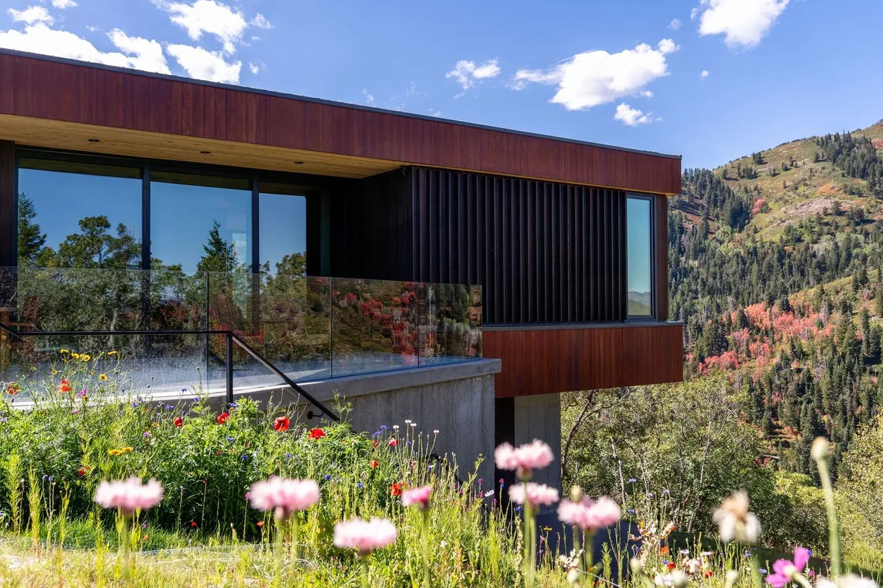 Modern house exterior with wood and black siding next to a mountain landscape and wildflower garden.