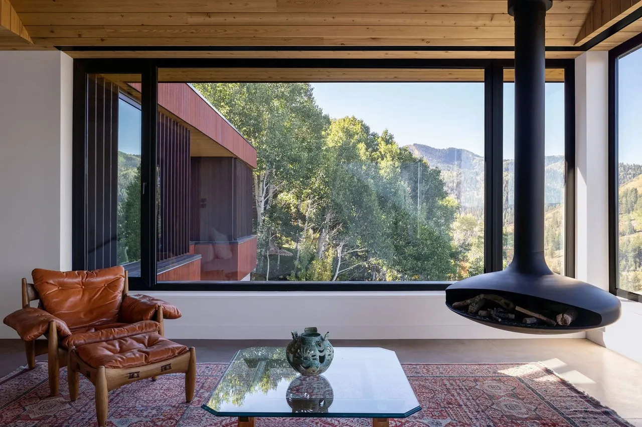 Living room with large floor-to-ceiling glazing offering expansive views to the wooded landscape and hills.
