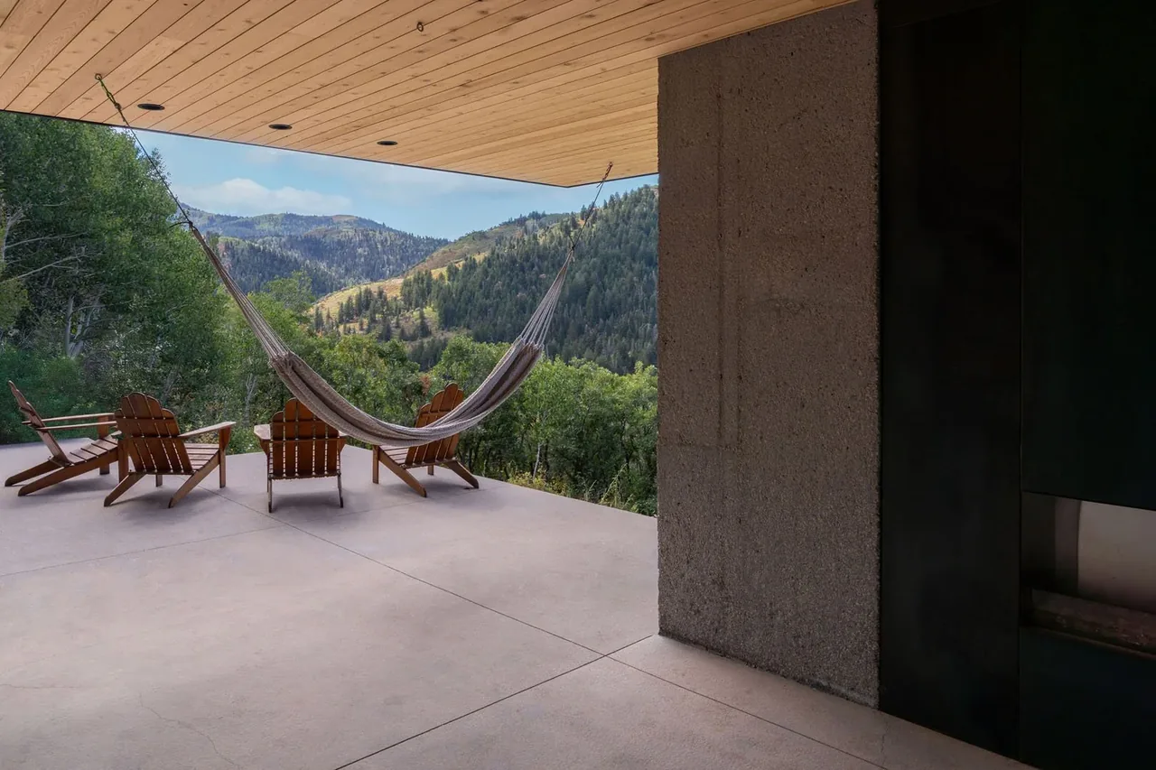 Outdoor patio with hammock and Adirondack chairs facing forested hills.