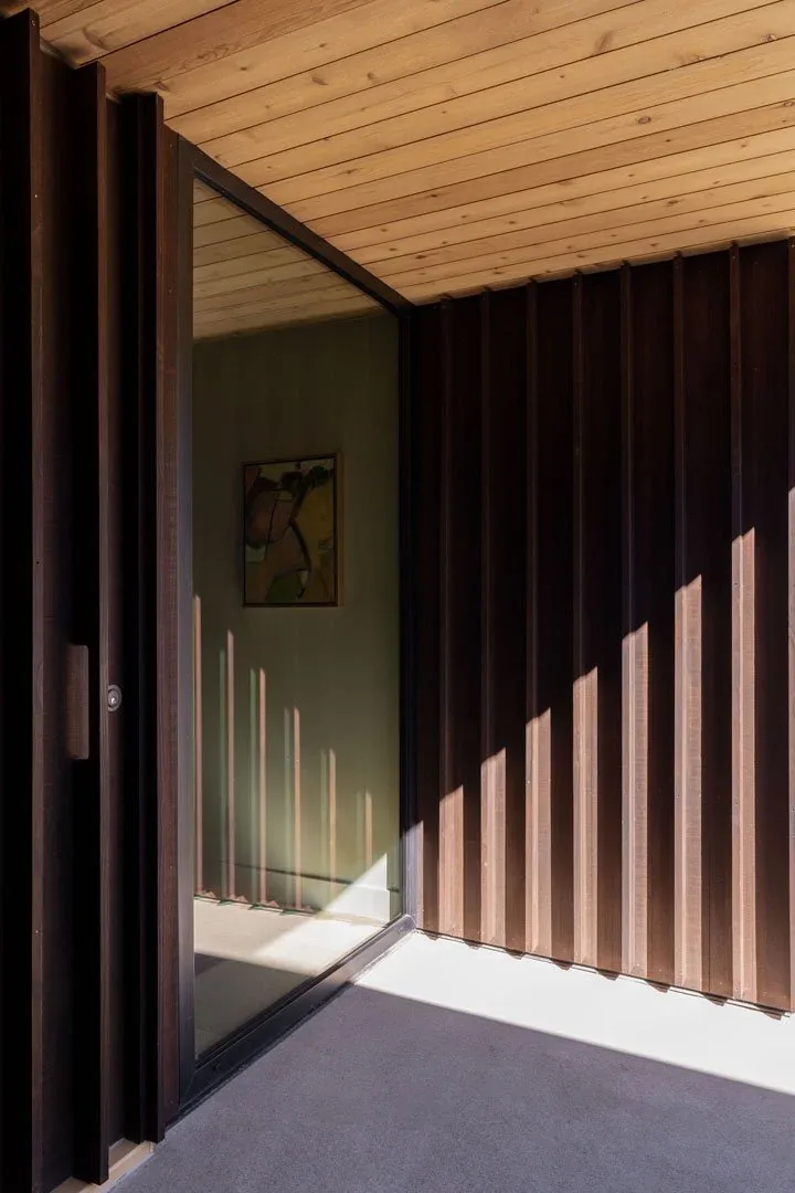 Modern exterior corner with vertical metal cladding, wood ceiling, and glass sliding door.