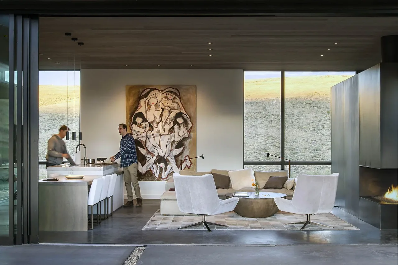 Open living area with a kitchen island, seating space, and large windows revealing the hillside outside.