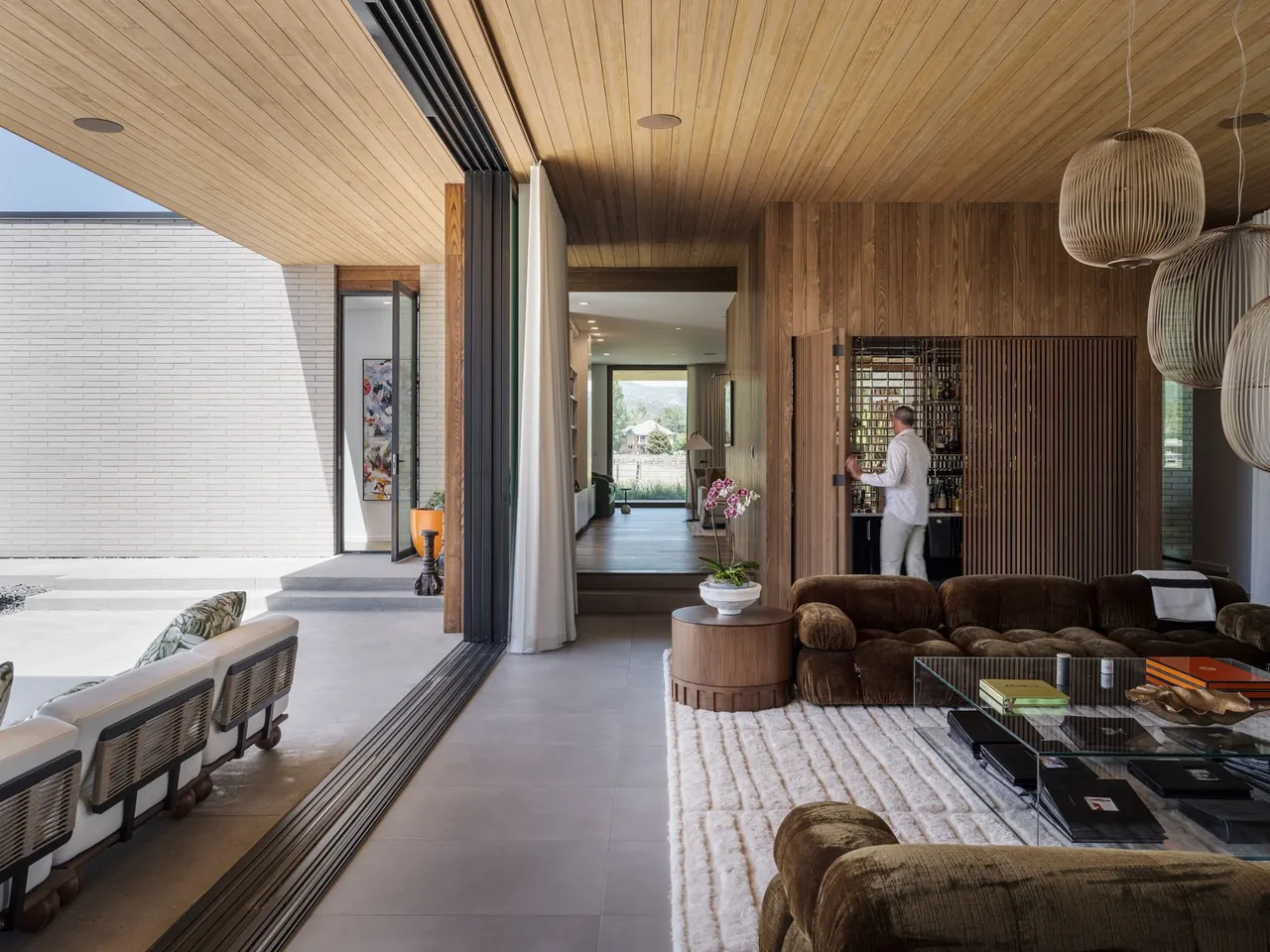 Living room with floor-to-ceiling glass doors open to covered patio, showing wood paneled ceiling and wall.