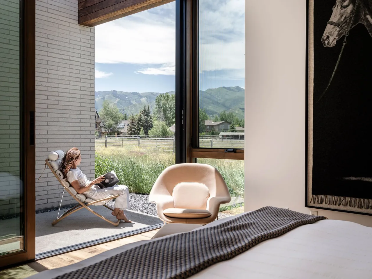 Bedroom with floor-to-ceiling glazing and sliding glass door opening to a patio with a lounge chair.