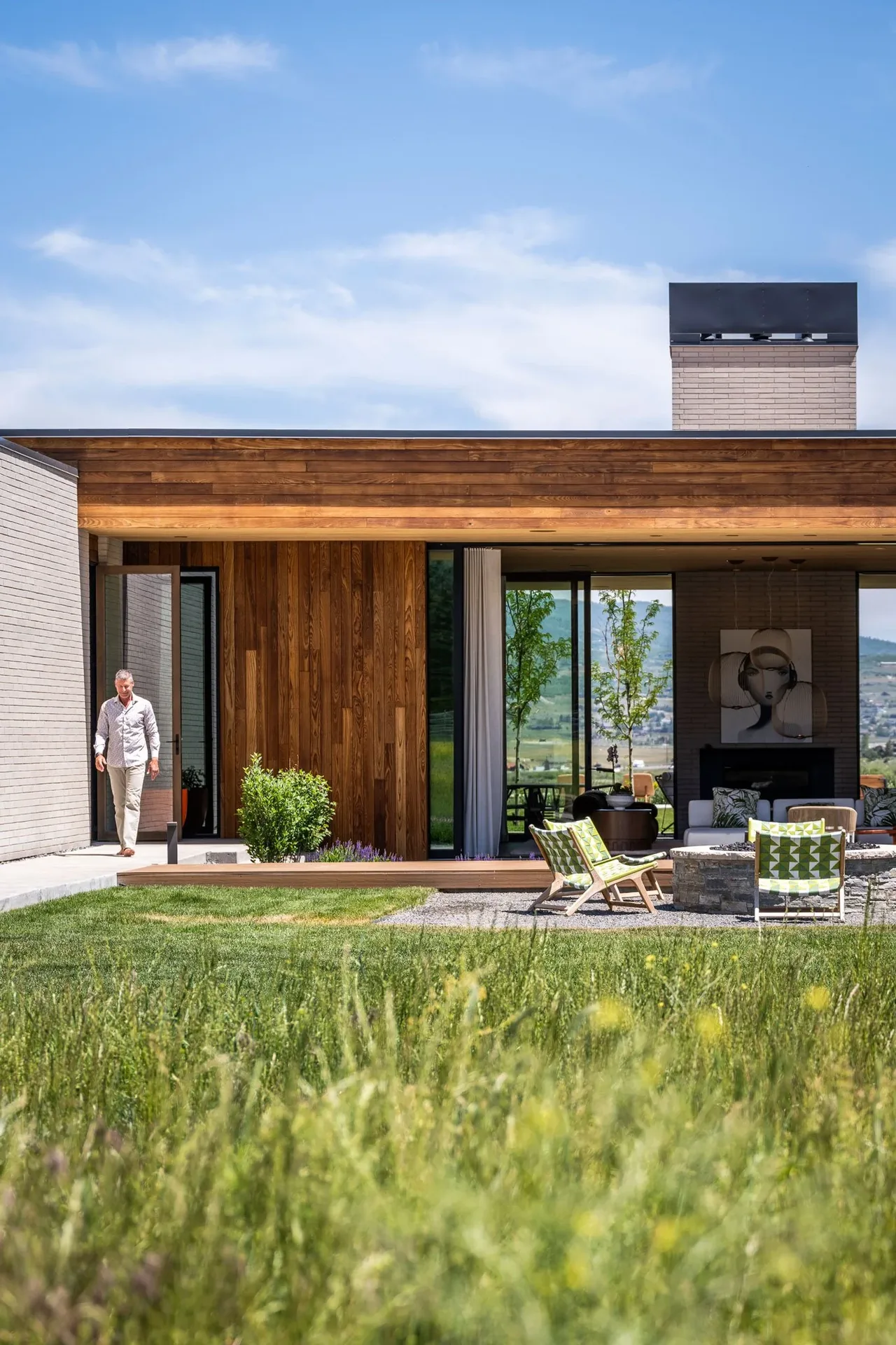 Exterior of a modern single-story house featuring wood cladding, stucco walls, floor-to-ceiling glazing, and a covered patio.