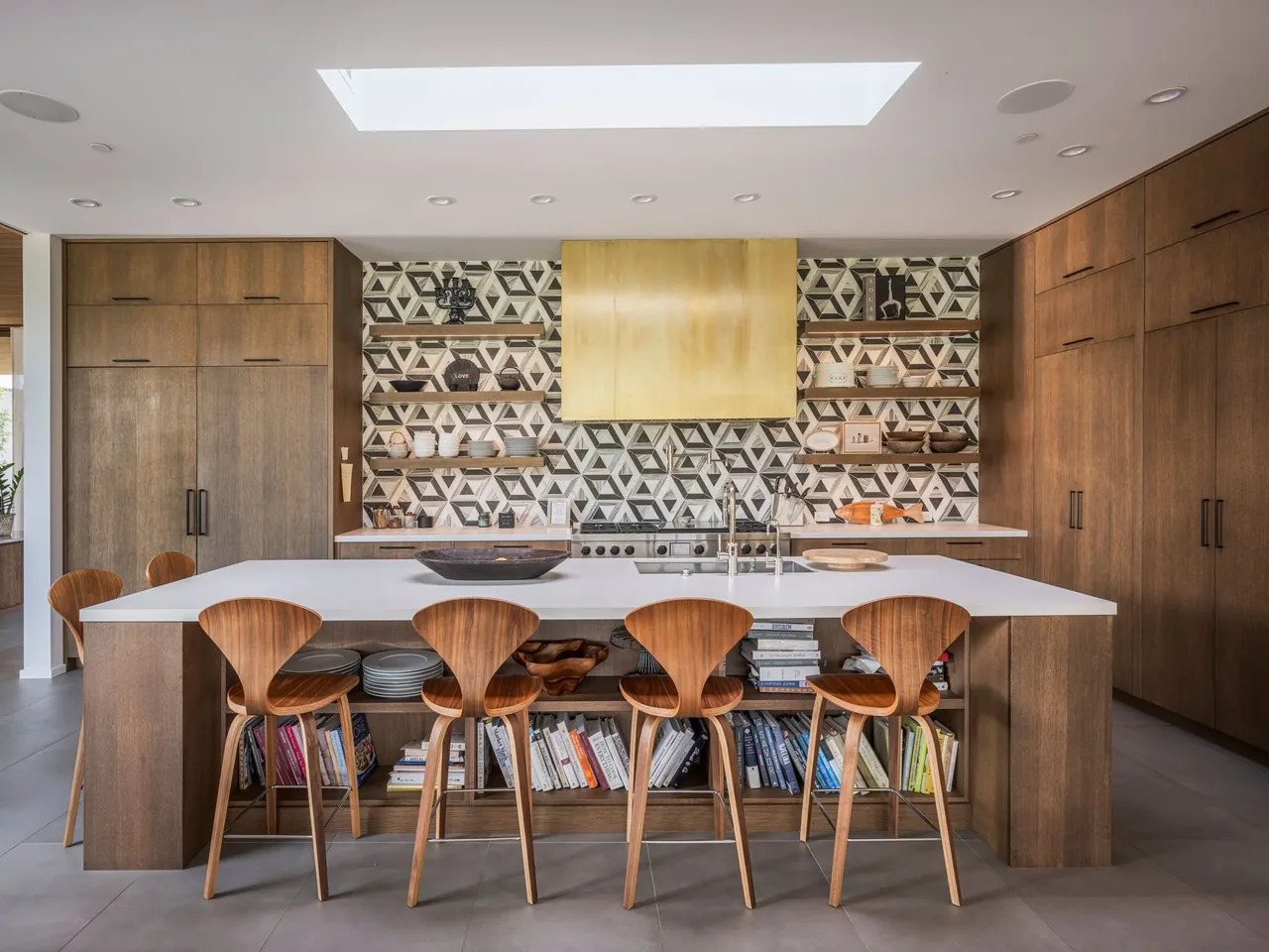 Kitchen with a white island, wooden bar stools, geometric tile backsplash, and wood cabinets beneath a skylight.