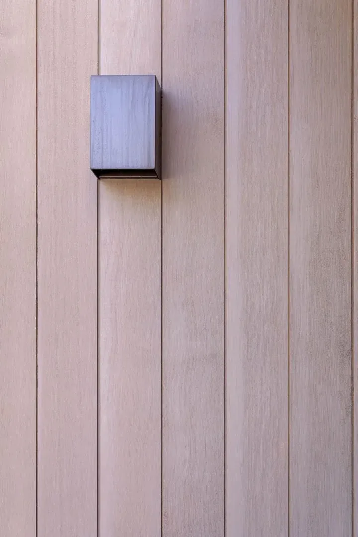 A light wood vertical panel wall features a dark, square wall-mounted light fixture.