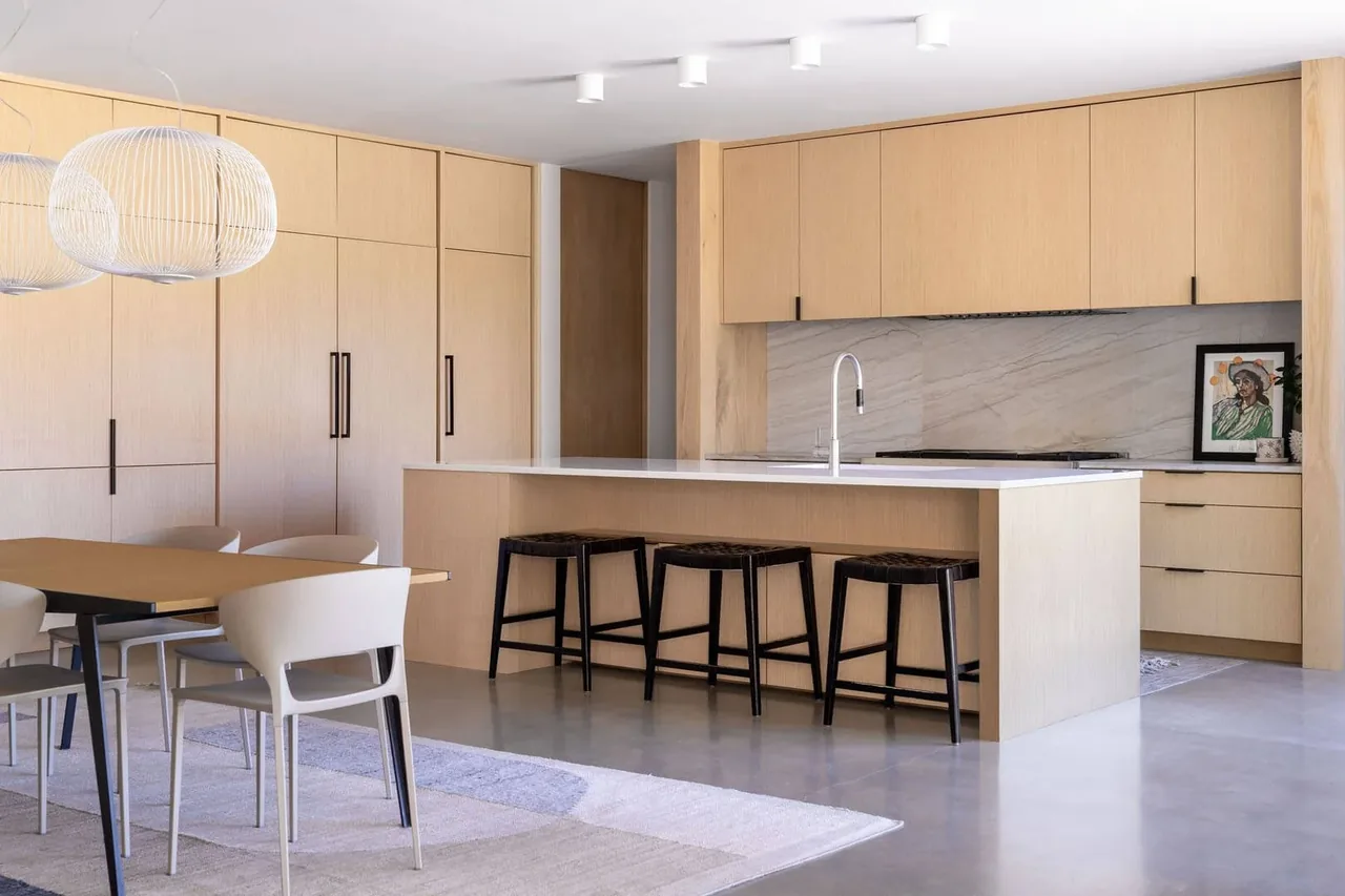 Open kitchen with light wood cabinets and island, white quartz countertop, and a dining table with seating for six.