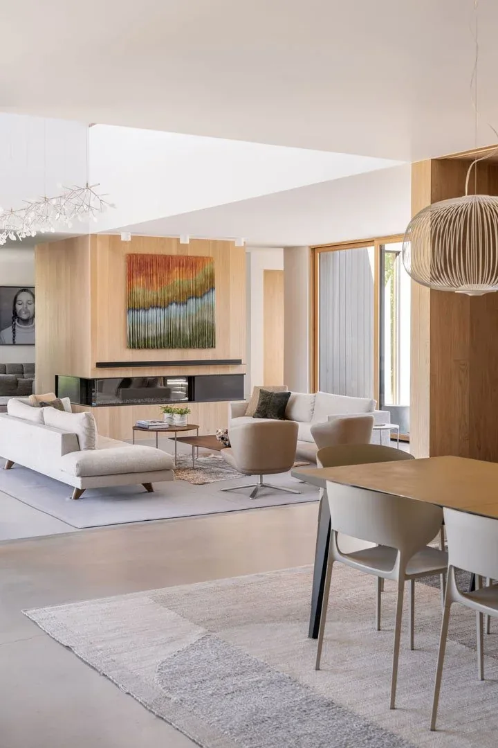 Living area with light wood panel walls, linear fireplace, abstract wall art, and pendant lighting over the dining table.