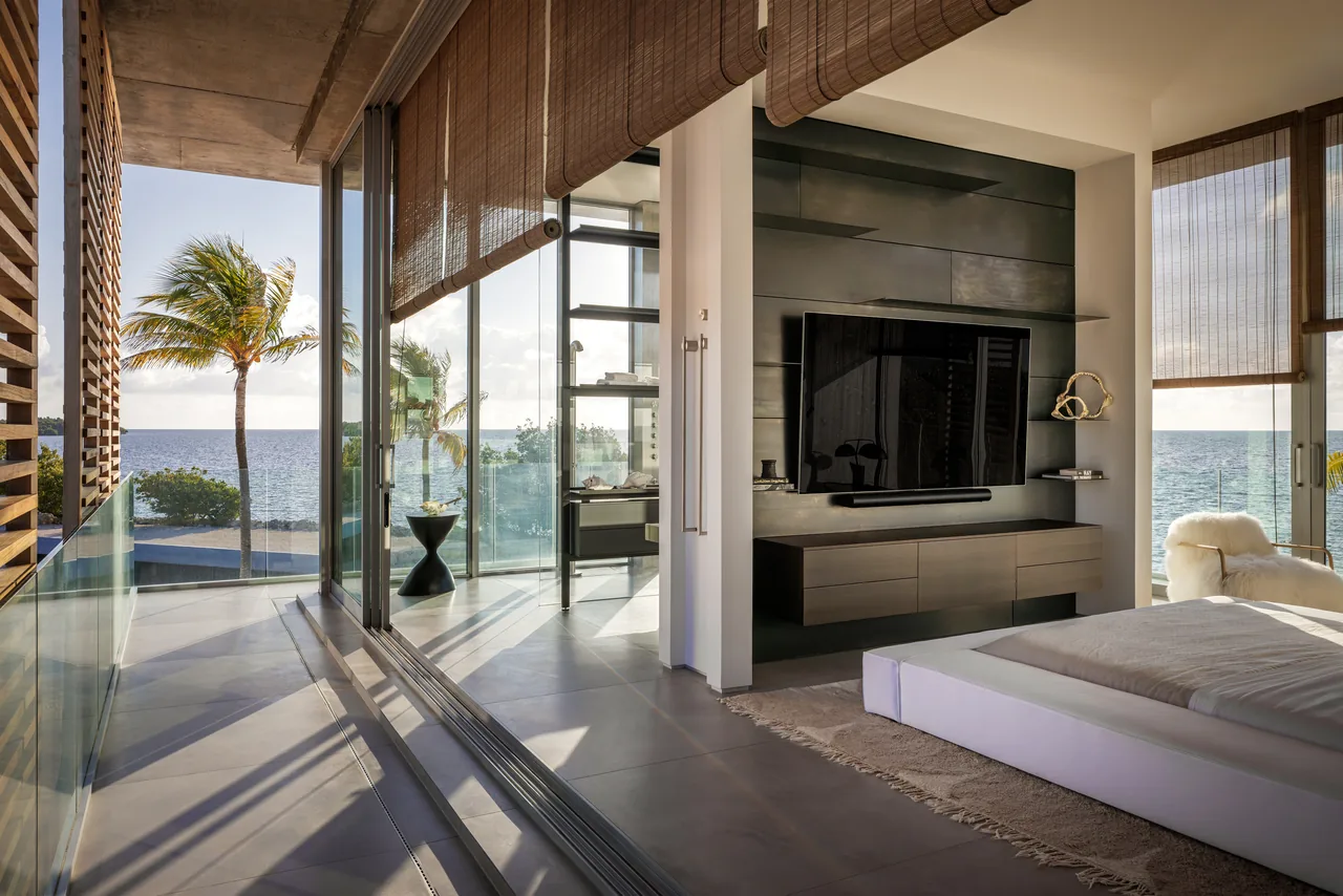 Bedroom with floor-to-ceiling sliding glass doors opening to a balcony with glass railing and ocean view.