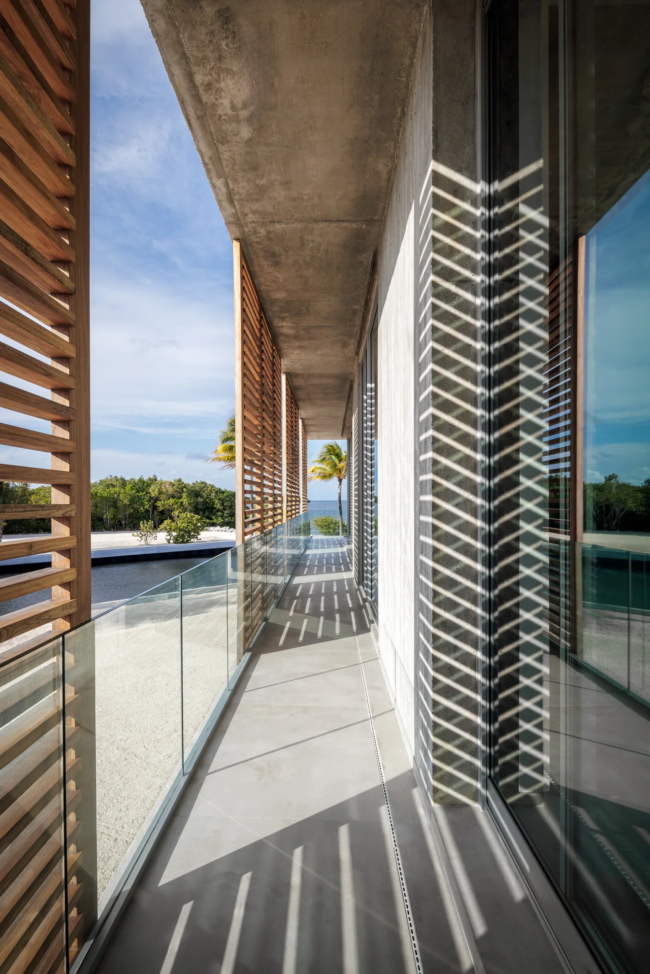Balcony featuring concrete ceiling, wood slat screens, and glass railing with waterfront views.