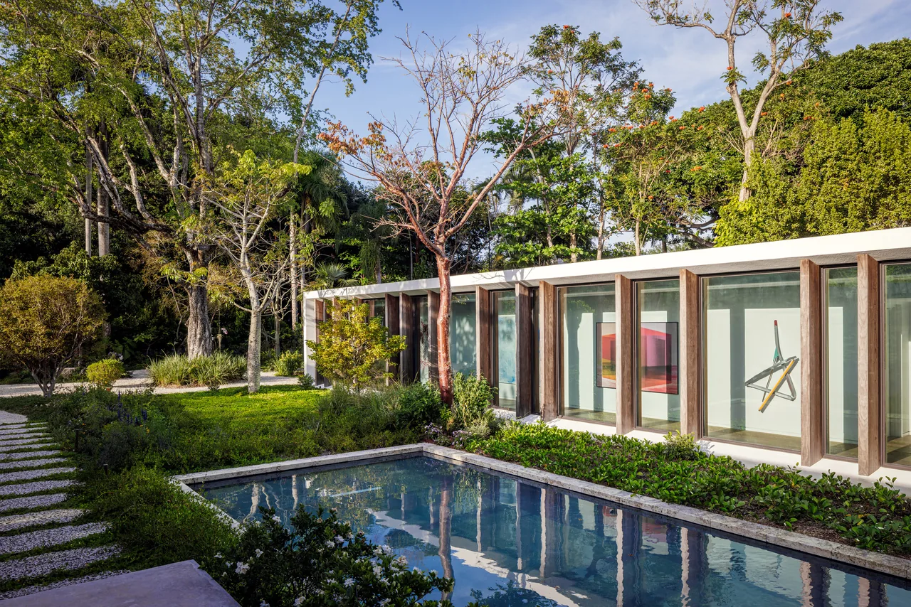 The Kiaora Residence features vertical wood posts framing large windows overlooking a reflecting pool and garden.