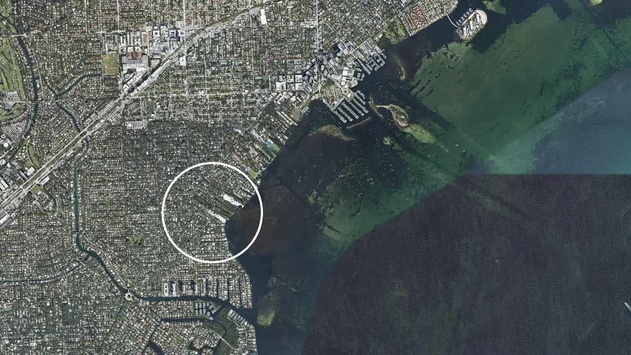 Aerial satellite view of a coastal neighborhood near Miami with a white circle highlighting a specific area adjacent to the water.