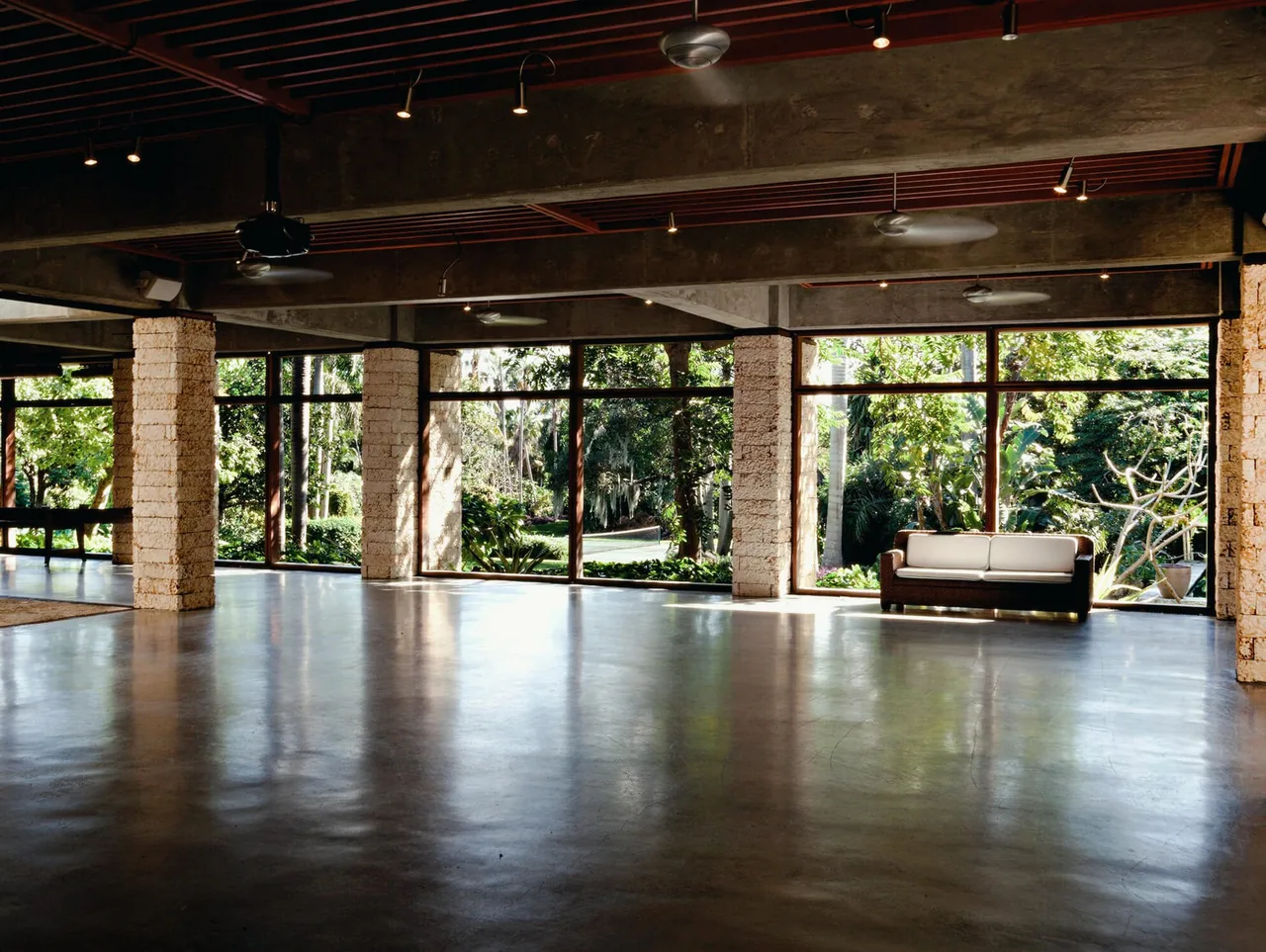 Interior view of a spacious room featuring stone columns and floor-to-ceiling glazing overlooking a green garden.